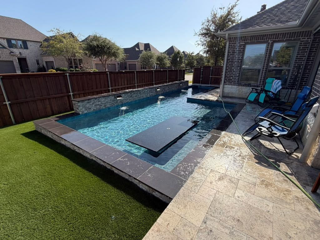 Modern swimming pool with integrated spa, stone patio, and artificial turf